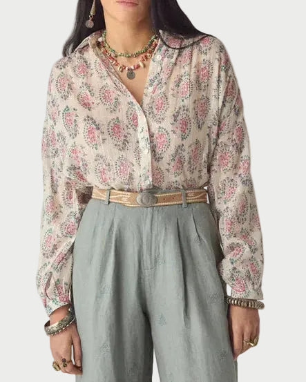 Woman wearing a floral blouse and light green pants on a plain background