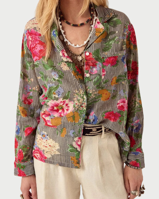 Person wearing a colorful floral and striped jacket with beige pants on a plain background