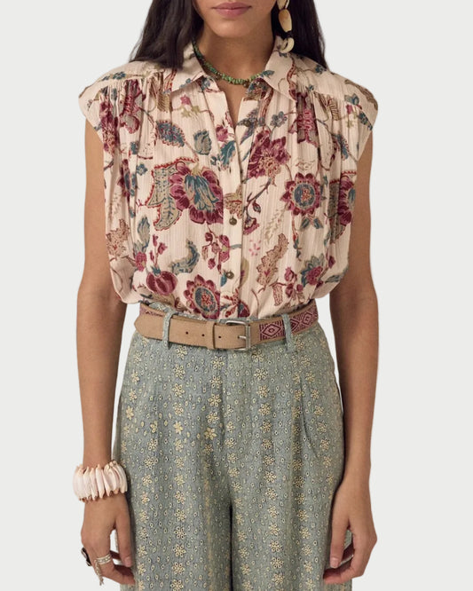 Woman wearing a sleeveless floral blouse and patterned pants against a plain background