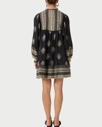 Person wearing a black dress with white patterns on a plain background