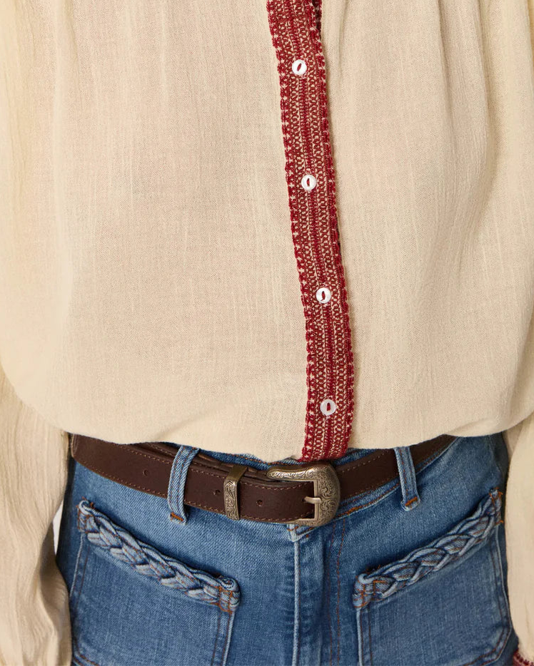Beige blouse with red embroidery and blue jeans on a plain background