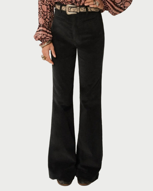 Person wearing black flared pants with a patterned top on a plain background