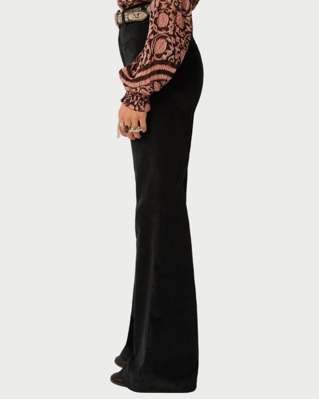 Person wearing a patterned top and black flared pants on a plain background