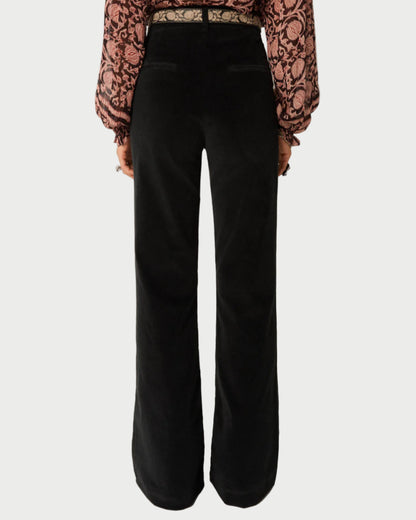 Person wearing black flared pants with a patterned top on a plain background