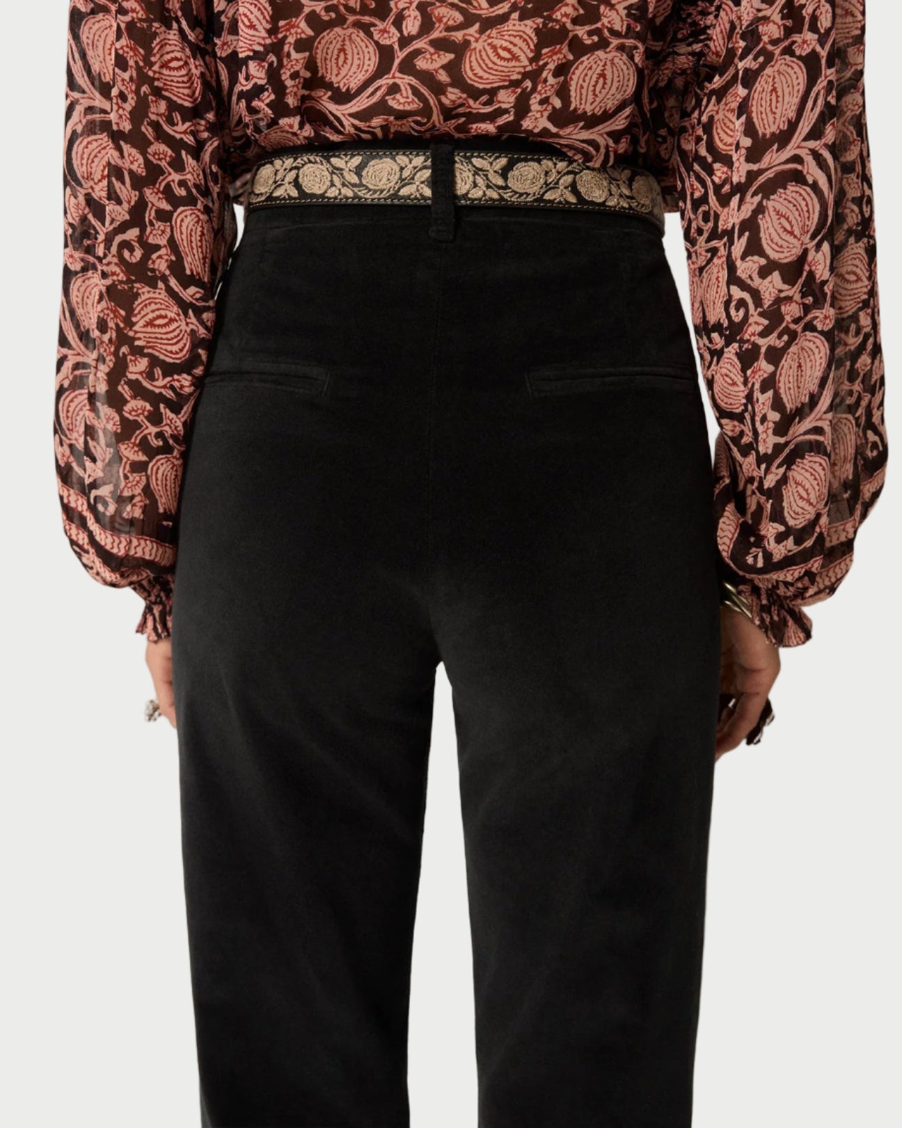 Person wearing a patterned blouse and black pants against a neutral background