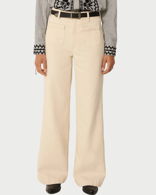 A person models Maison Hotel Hamlet Pants—high-waisted, wide-leg cream trousers with front patch pockets—styled with a black belt, black and white patterned long-sleeve shirt, and black shoes. Image is cropped at the shoulders.