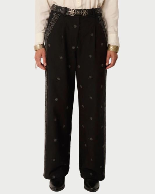 Person wearing black pants with white polka dots and a white shirt on a plain background