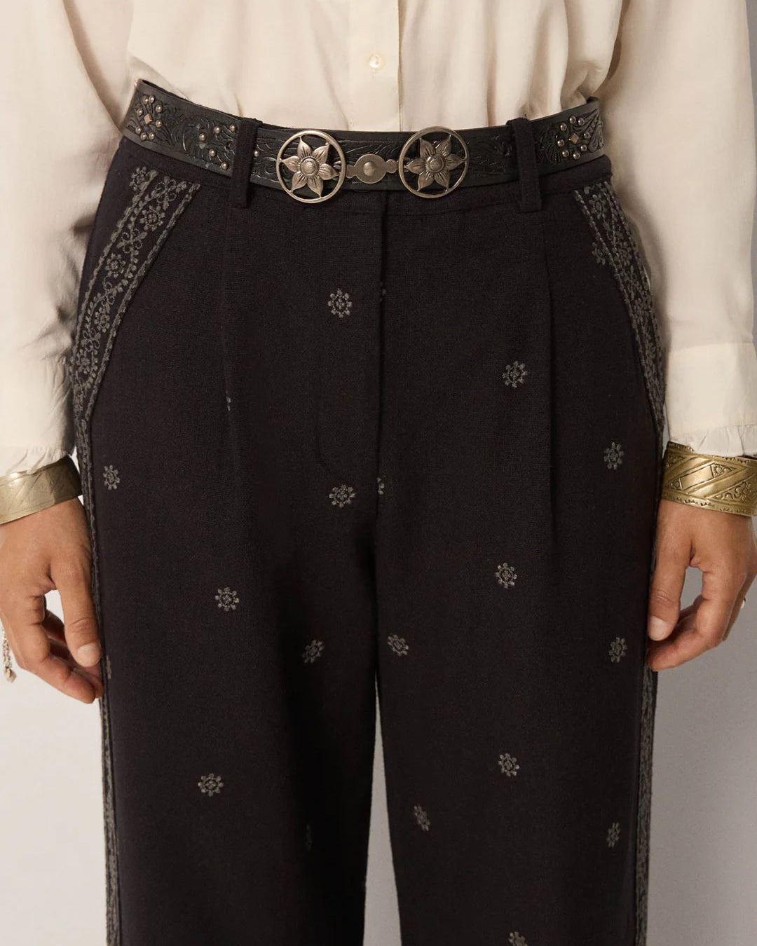 Black pants with floral embroidery and a belt, worn by a person.
