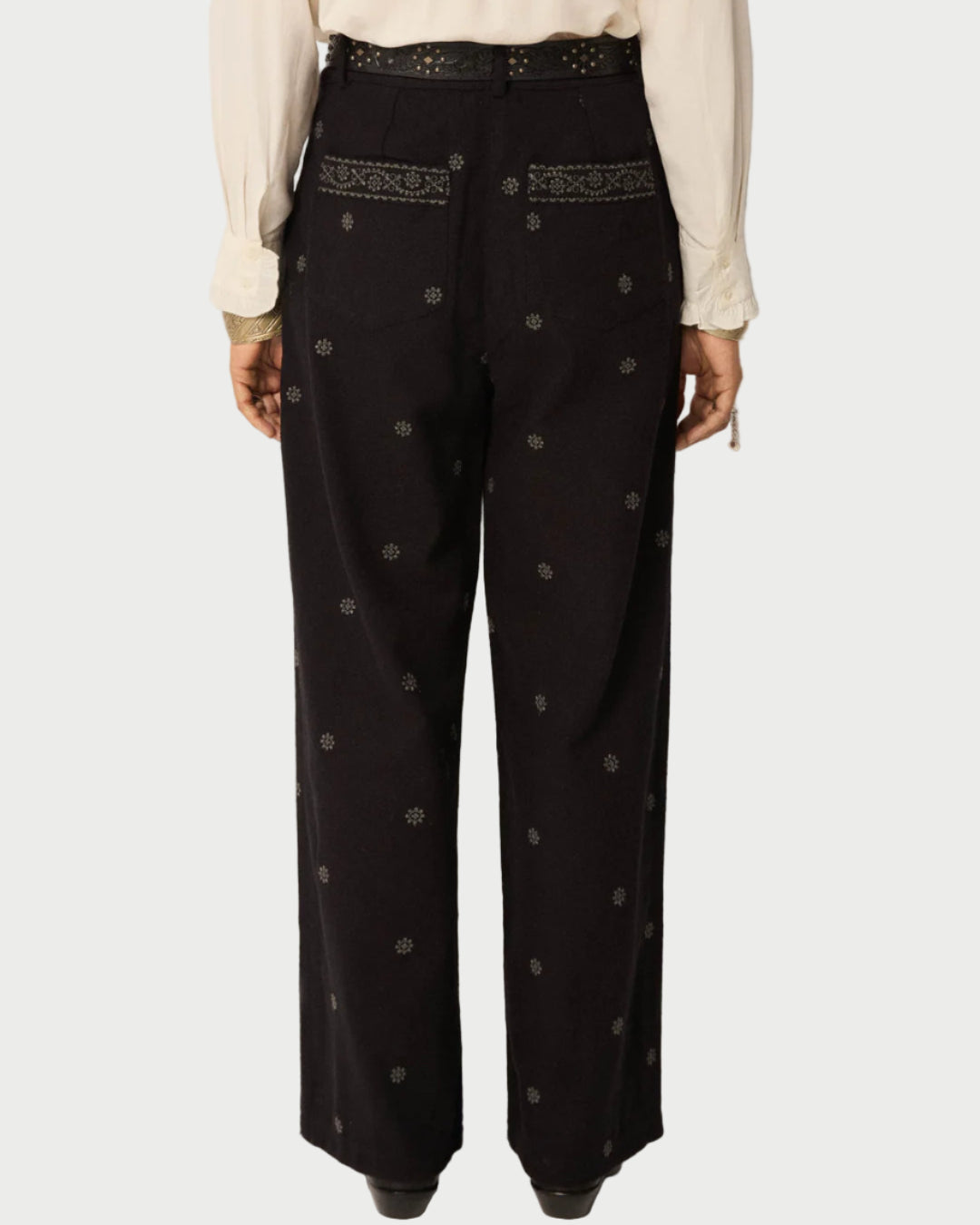 Black pants with embroidery and buttons worn by a person on a plain background