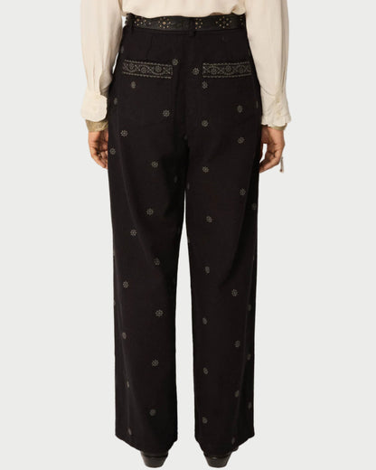 Black pants with embroidery and buttons worn by a person on a plain background