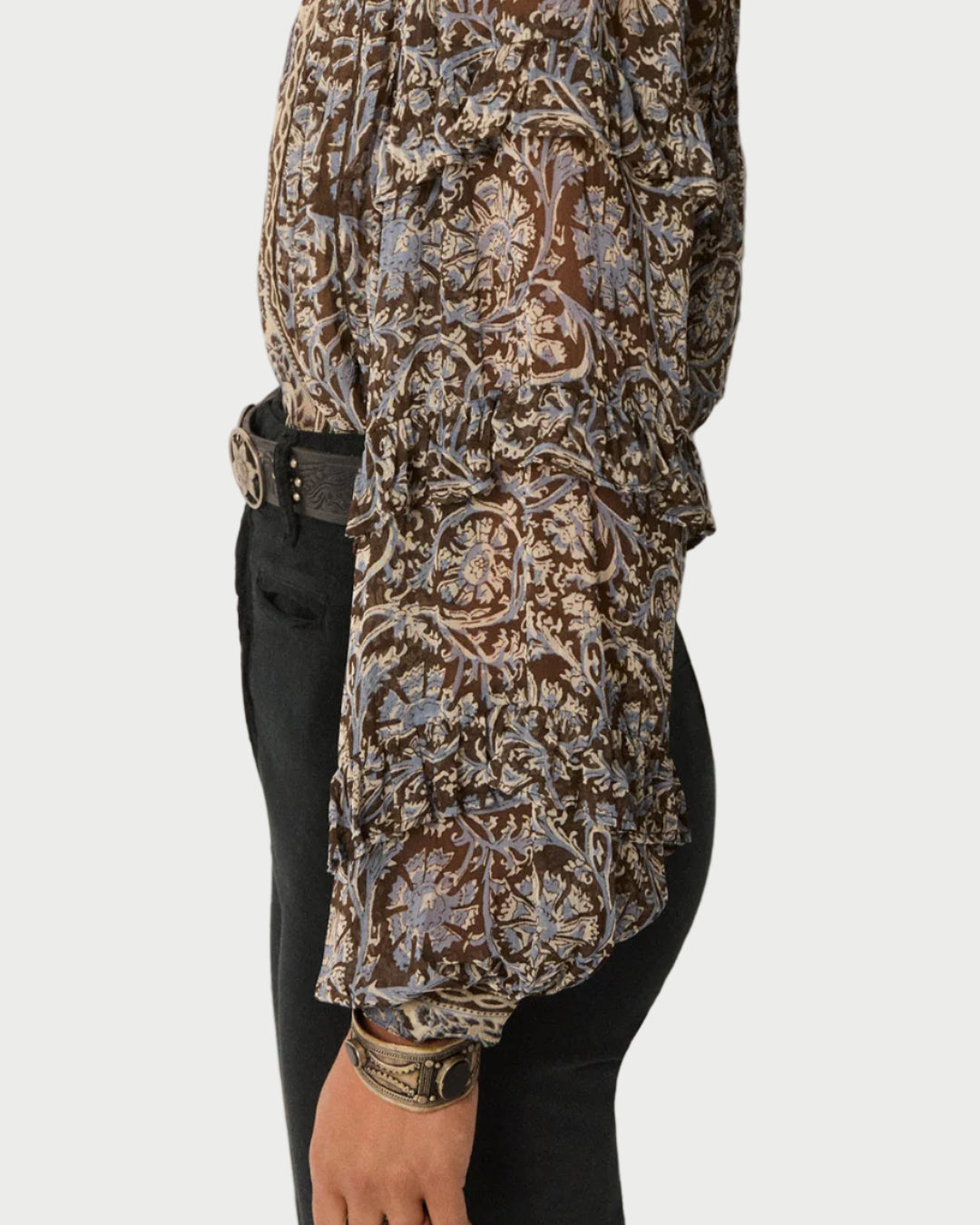 Person wearing a patterned long-sleeve top and black pants on a plain background