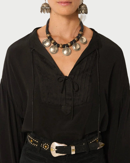 Person wearing a black top with a decorative necklace and belt against a neutral background