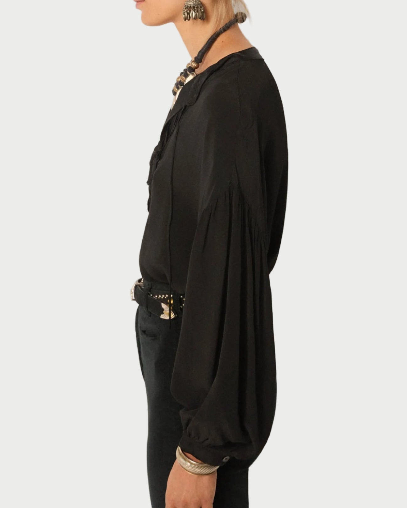 Person wearing a black blouse with long sleeves and a belt, standing against a plain background.