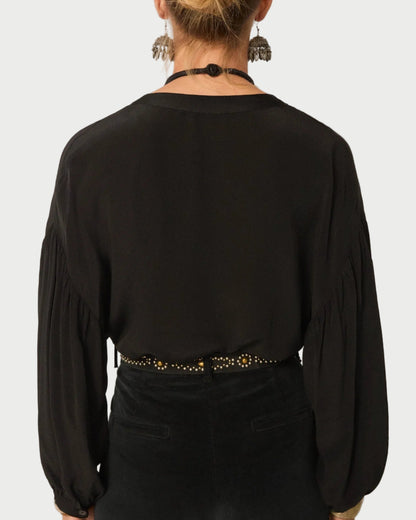 Person wearing a black blouse with long sleeves and a belt against a plain background