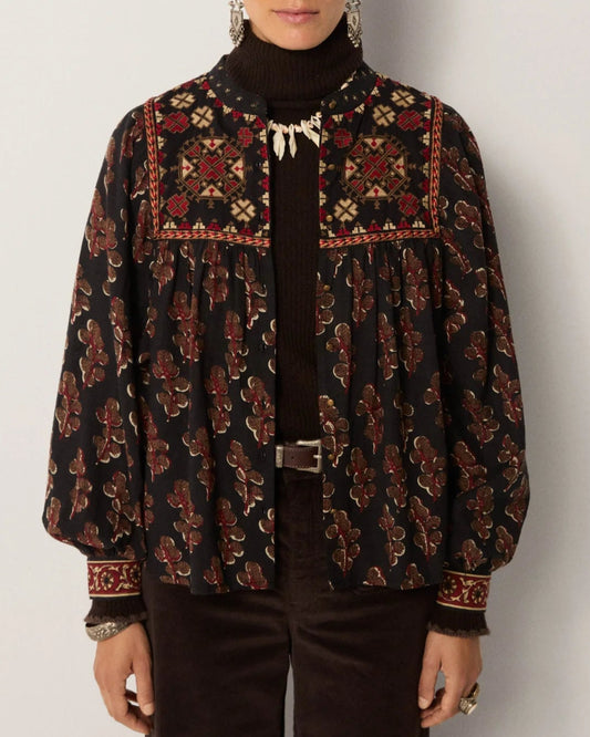 Woman wearing a patterned blouse over a black turtleneck against a plain background