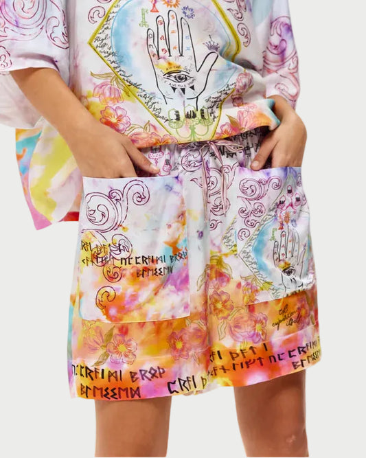 A person wears ME369 Kori Shorts and a matching loose-fit top with abstract patterns, a hand with an eye illustration, runic text, large pockets, and watercolor-inspired colors from the brand ME369.