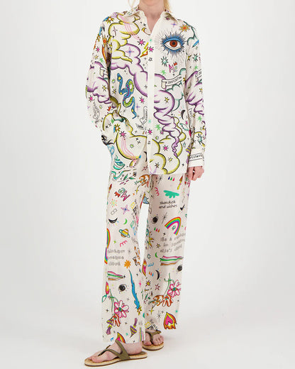 A person models ME369 Bailey Pants—loose-fitting pajama pants with playful, colorful prints of eyes, rainbows, stars, clouds, hearts, and flowers—against a plain white background, showcasing true dopamine dressing by ME369.