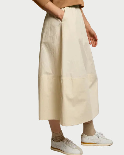 Someone wearing the Perfectwhitetee Minka Poplin Skirt Sugar by perfectwhitetee, paired with beige socks, white sneakers, and a light brown top stands against a plain white background.