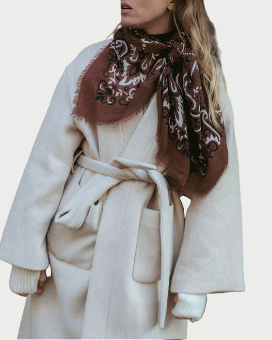 Woman wearing a white coat and patterned scarf against a wooden door and green wall.