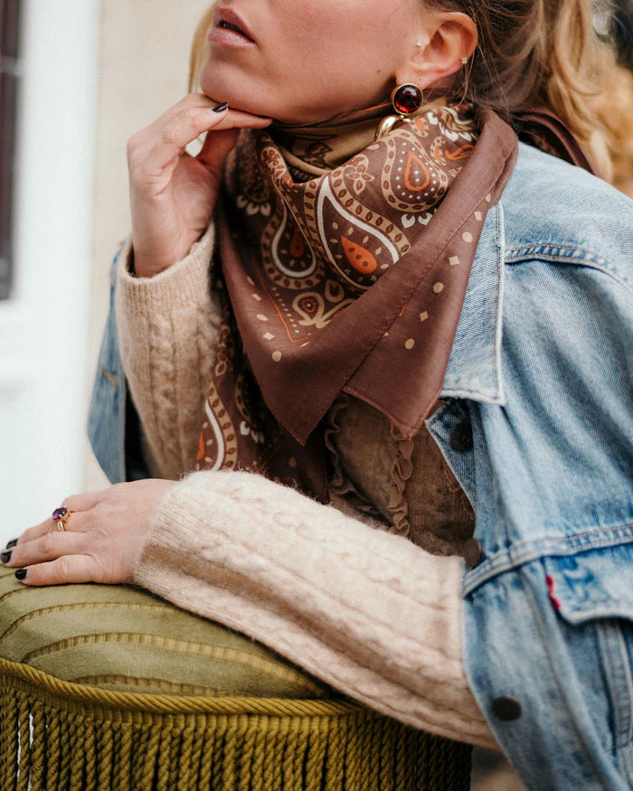 Woman wearing a patterned scarf and denim jacket sitting on a bench.