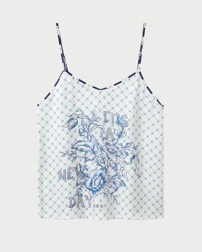 The ME369 Angelique Camisole is a white top with thin straps, showcasing a blue geometric check print and an intricate blue floral design on the front. Inspired by the original style, this camisole also features the phrase "IT'S A NEW DAY" printed in blue among the flowers.