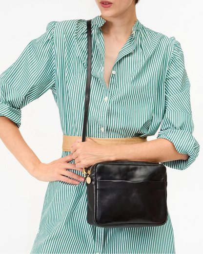 Woman wearing a green striped shirt and holding a black bag against a white background