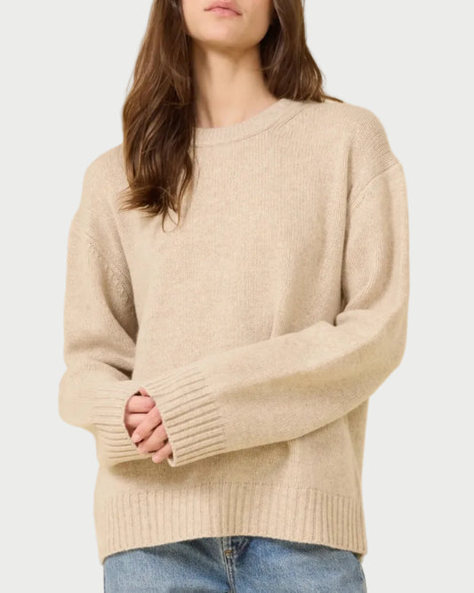 Woman wearing a beige sweater and blue jeans against a beige background