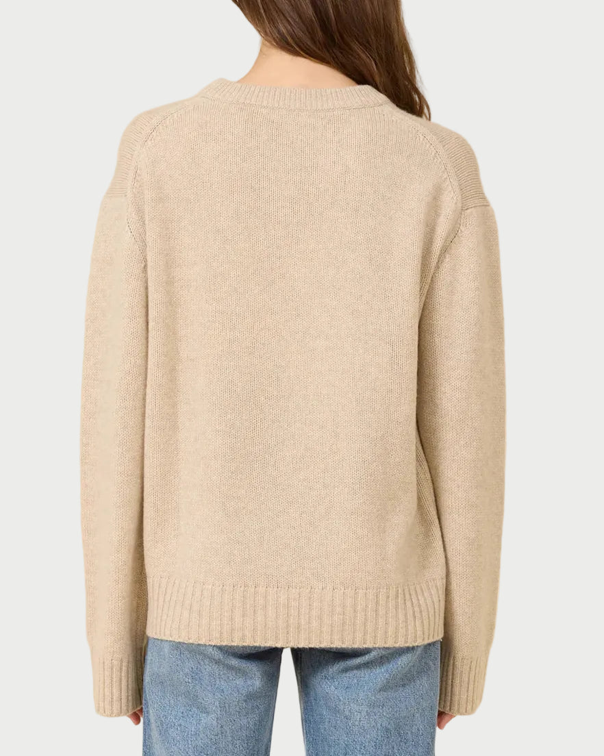 Person wearing a beige sweater and blue jeans on a beige background