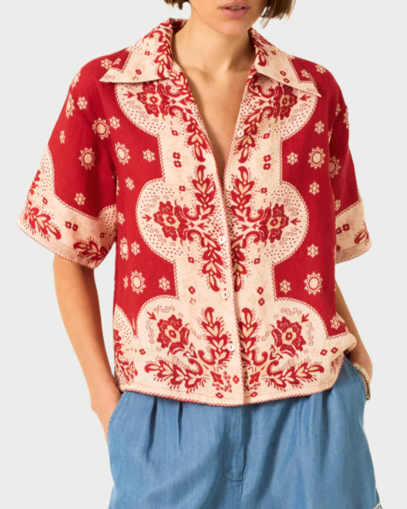 A person wears the Alix of Bohemia Stevie Short Sleeve Shirt, featuring a red and cream bandana-style print, paired with light blue high-waisted pants. The image is cropped above the nose.