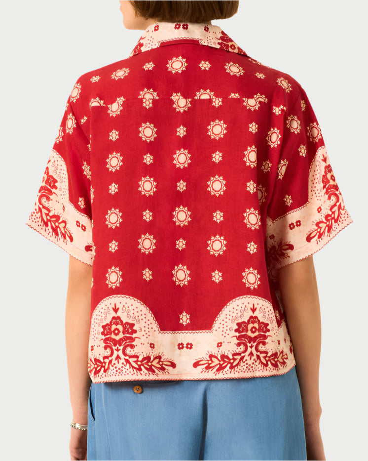A person is shown from the back wearing the Stevie Short Sleeve Shirt by Alix of Bohemia—a red top with a white bandana-inspired print—paired with light blue pants, set against a plain background.