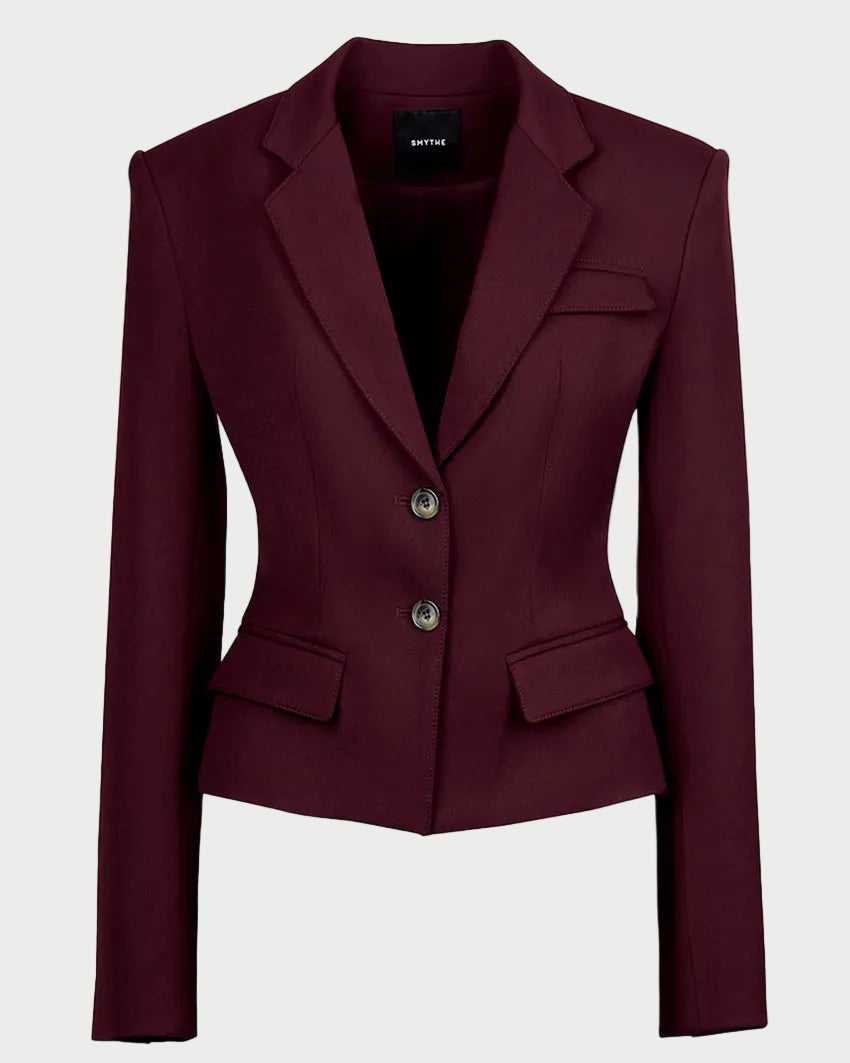 A cropped, structured blazer in deep burgundy with notched lapels, two front buttons, and flap pockets, shown on a plain light gray background.