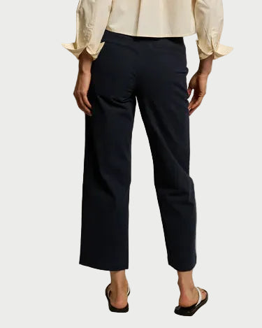 A person stands facing away, wearing a cream long-sleeve top, black Perfectwhitetee Pia Twill Pant by perfectwhitetee, and black sandals against a plain light background.
