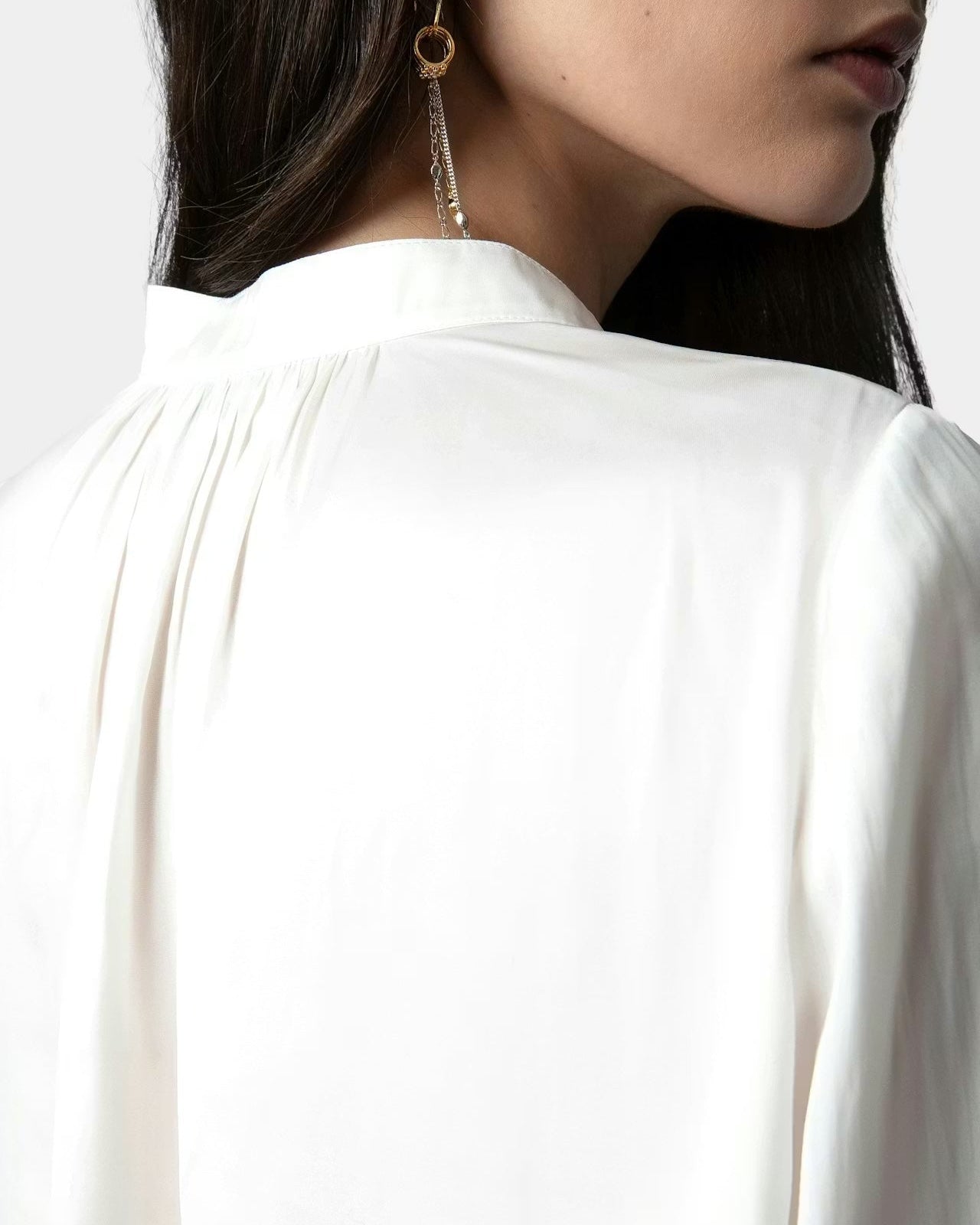 Close-up of a person wearing a white blouse with a plain background