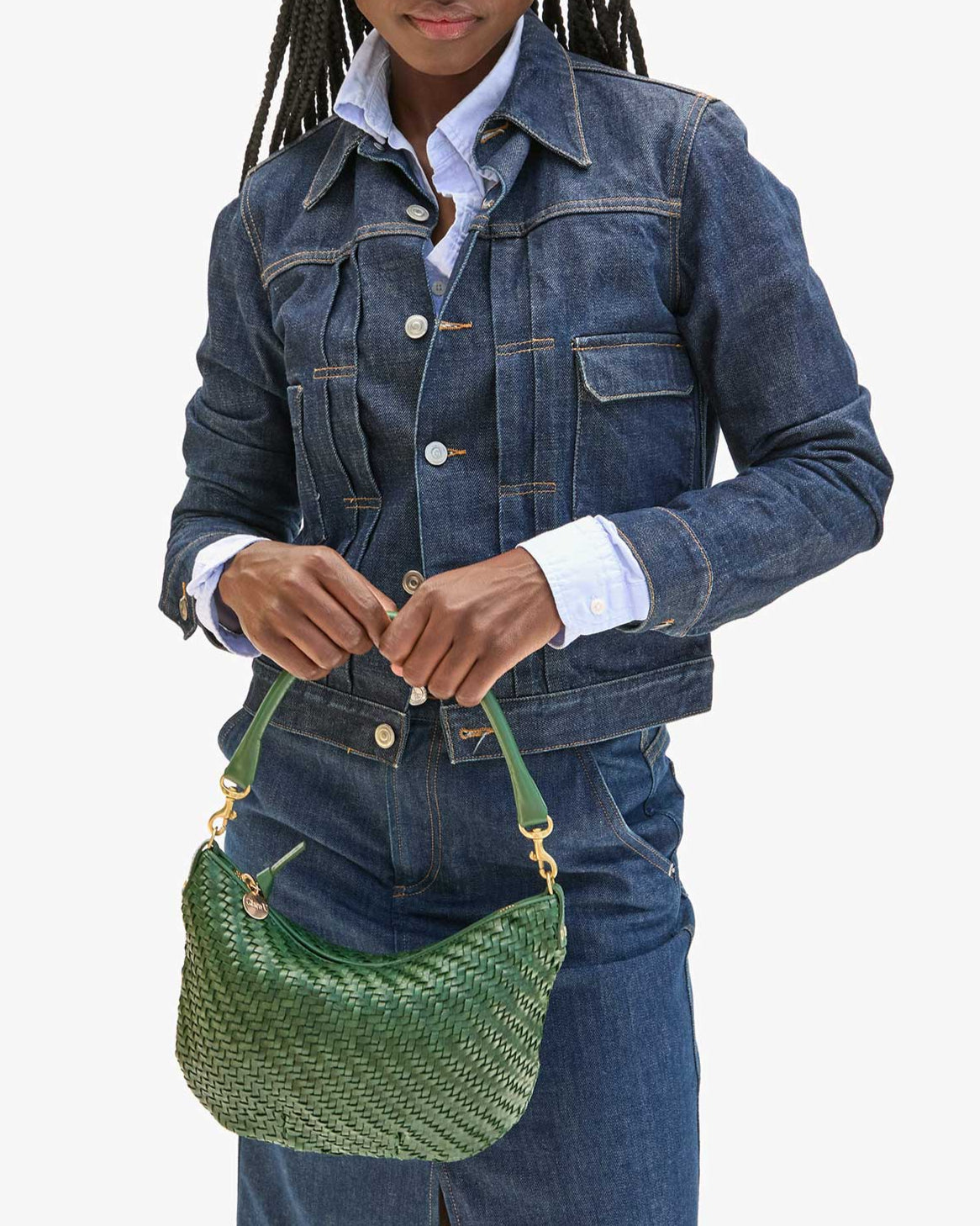 Person wearing a blue denim jacket holding a green handbag on a white background