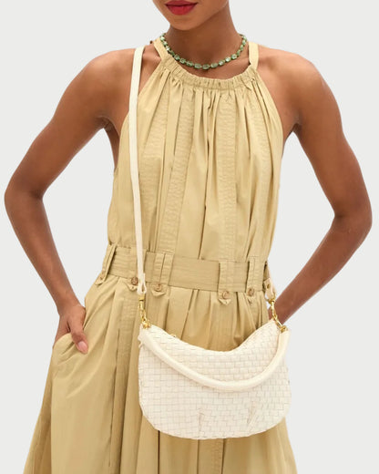 Woman wearing a beige dress with a white handbag against a plain background