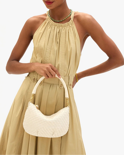 Woman in a beige dress holding a white handbag against a white background