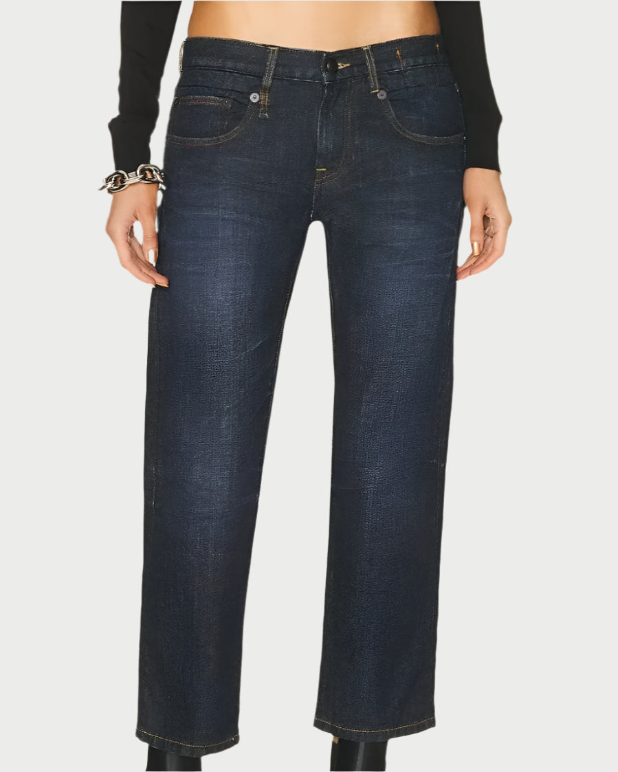 A person wearing R13 Boy Straight Jeans in Avery Indigo, paired with black chunky platform boots, is standing against a plain white background. They are also wearing a long-sleeved black top and have a bracelet on their left wrist. The cropped jeans reveal a bit of their ankles.