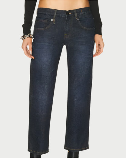 A person wearing R13 Boy Straight Jeans in Avery Indigo, paired with black chunky platform boots, is standing against a plain white background. They are also wearing a long-sleeved black top and have a bracelet on their left wrist. The cropped jeans reveal a bit of their ankles.