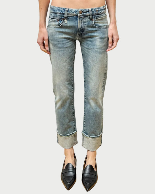 Person wearing light blue jeans and black shoes standing against a textured white wall.