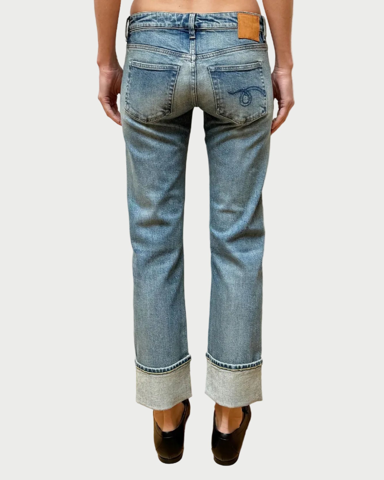 Person wearing light blue jeans with a white brick wall background