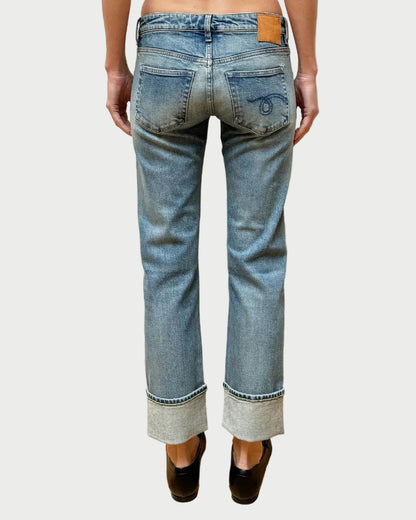 Person wearing light blue jeans with a white brick wall background