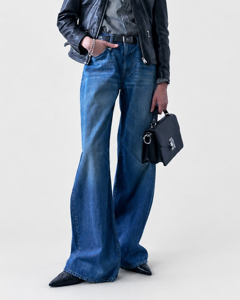A person wearing a leather jacket and R13 D’Arcy Flare Jean, holding a black handbag.