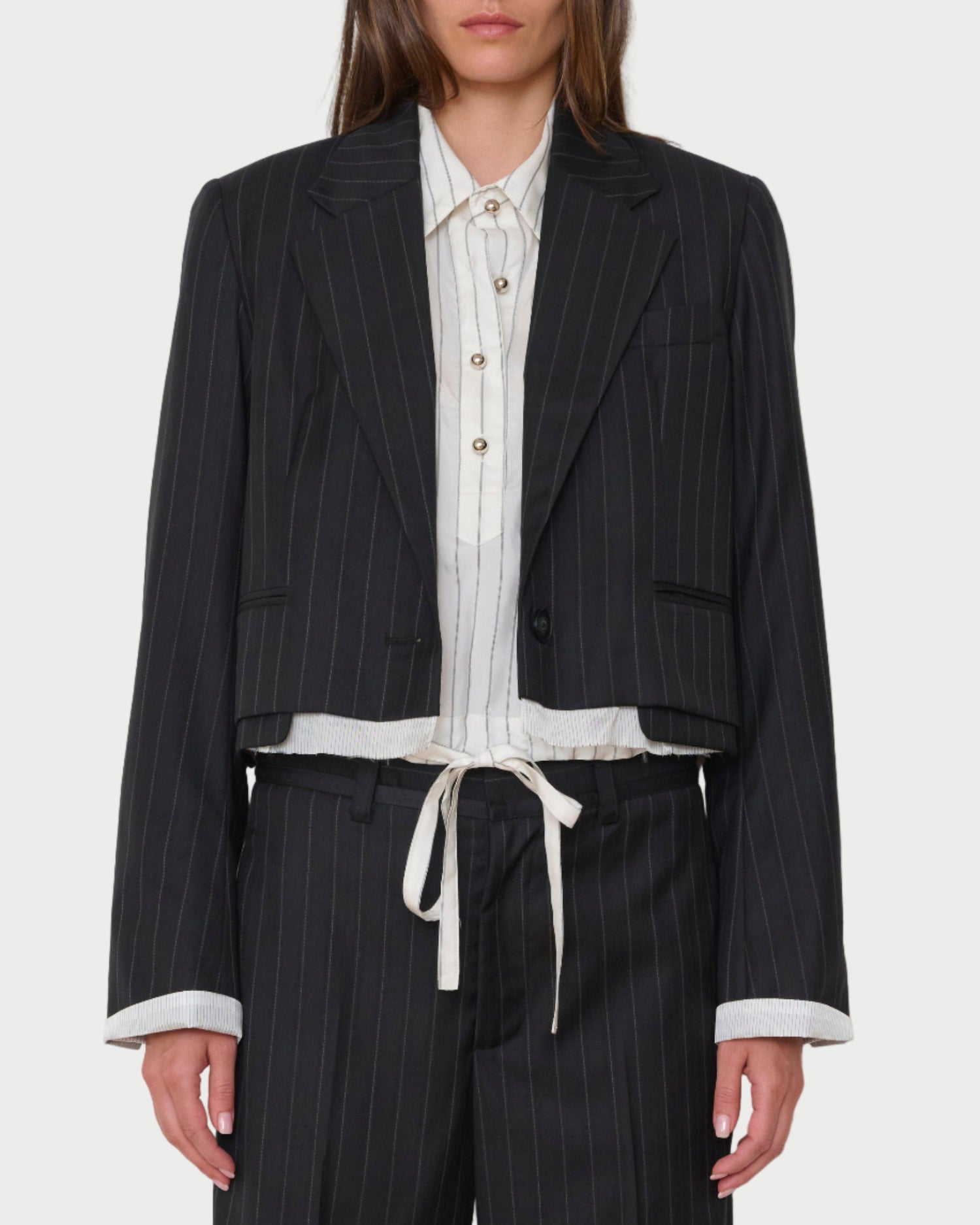 Woman wearing a black pinstripe suit with a white shirt and tie on a light gray background