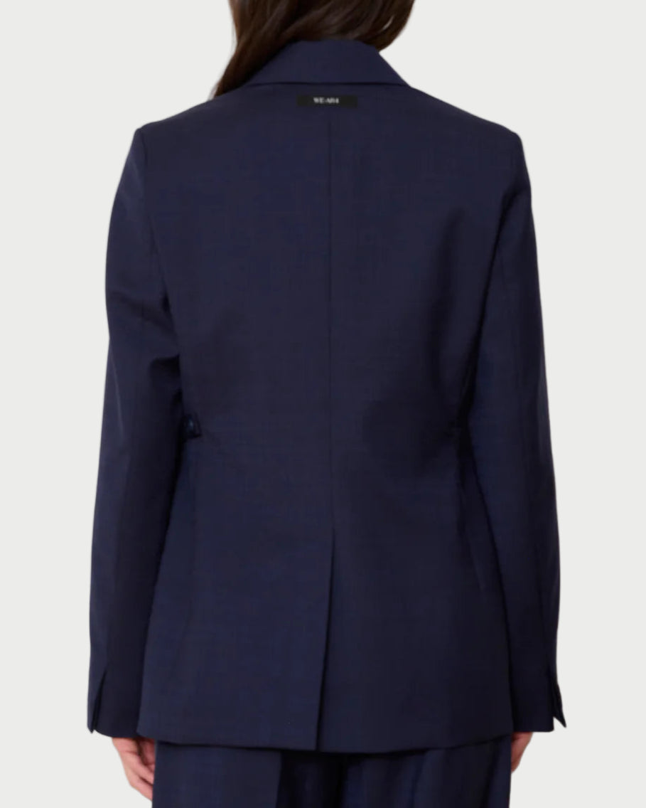 A person with long dark hair is seen from behind wearing the WE-AR4 Smoking Blazer by WE-AR4, paired with matching pants, against a plain light gray background.