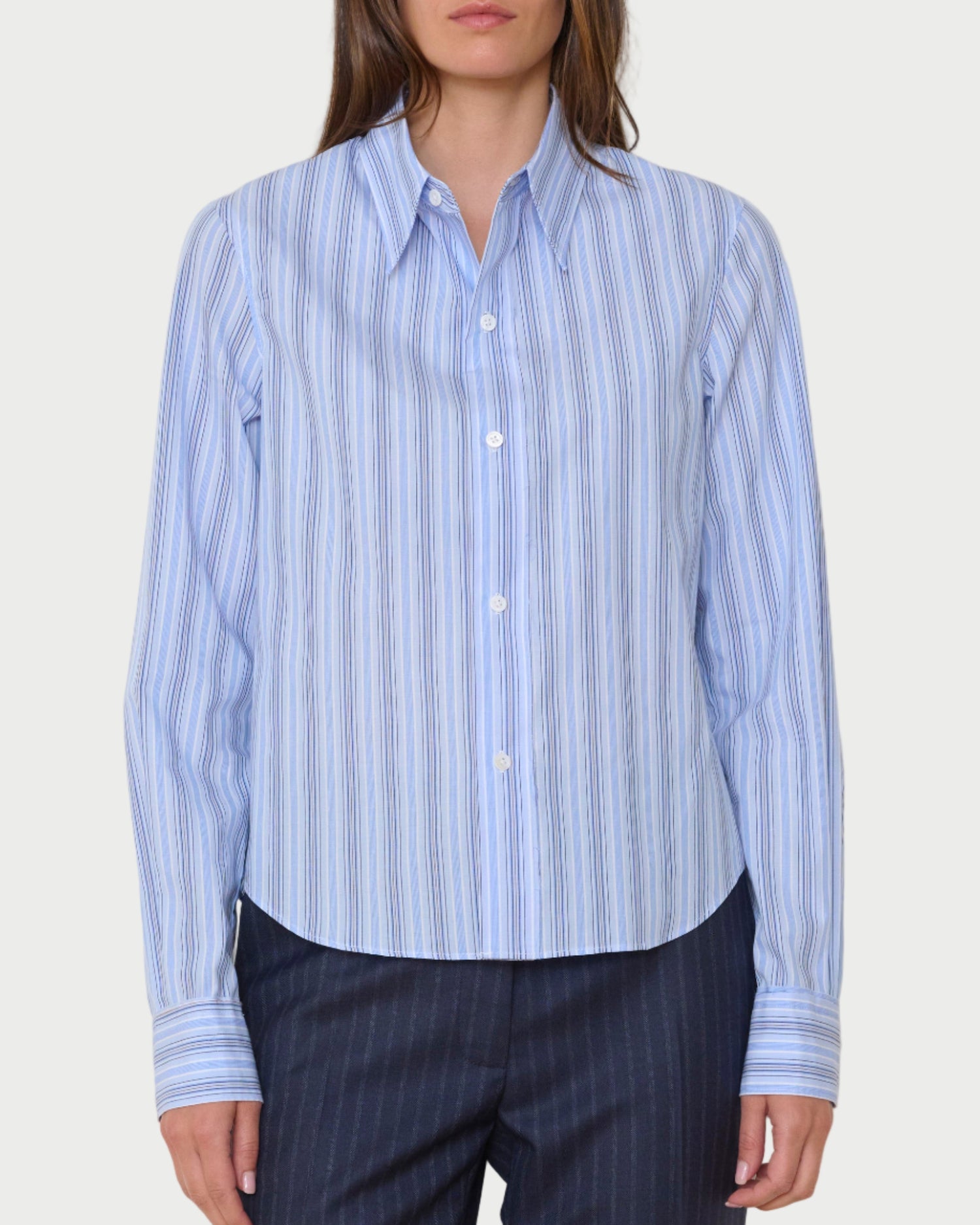 Woman wearing a light blue striped shirt and dark pants against a white background