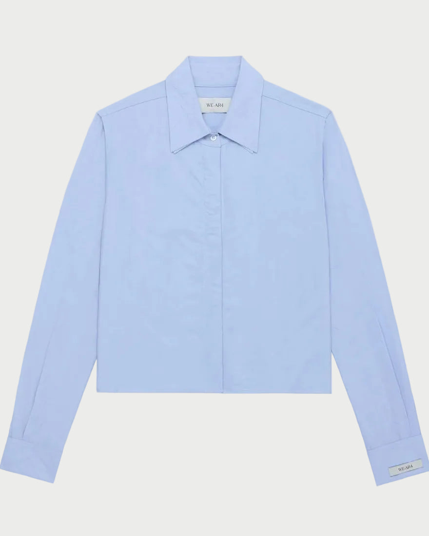 The WE-AR4 Campbell Shirt by WE-AR4 is a light blue, long-sleeve modern button-down featuring a pointed collar and cuffs, displayed flat on a white background.