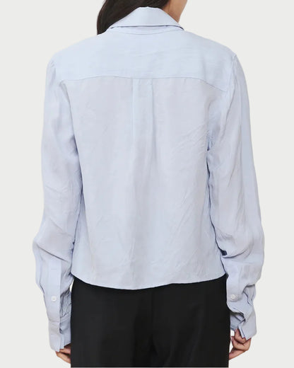 A person is shown from the back against a plain white background, wearing the WE-AR4 Campbell Shirt by WE-AR4 in light blue upcycled cotton with long sleeves, paired with black pants.