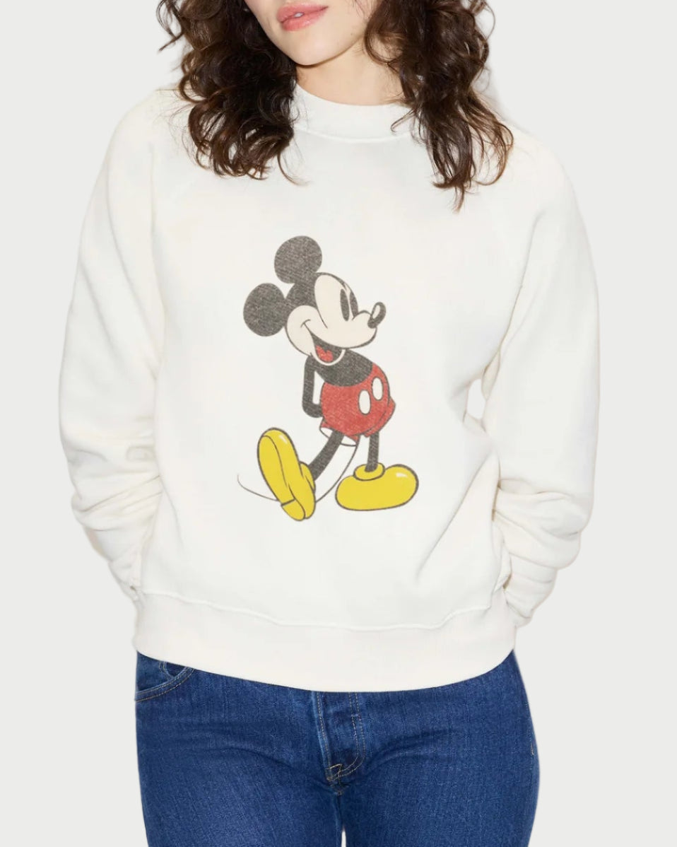 A person wears the RE/DONE Classic Crewneck Mickey Mouse sweatshirt, featuring a vintage-inspired Mickey graphic on the front, paired with blue jeans. The comfy French terry design is by RE/DONE, and the person's face is partially out of frame.