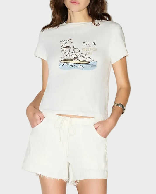A woman wears the RE/DONE Snoopy Hang Ten Classic Tee by RE/DONE with white drawstring shorts, hands in her pockets and standing against a plain background.