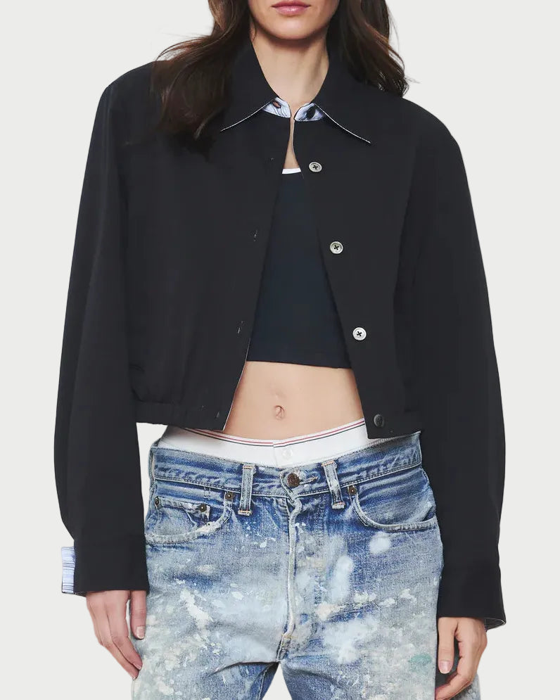 Woman wearing a black jacket and blue denim shorts on a plain background
